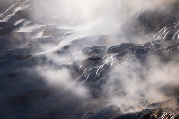 Steaming geothermal landscape with rocky terraces.