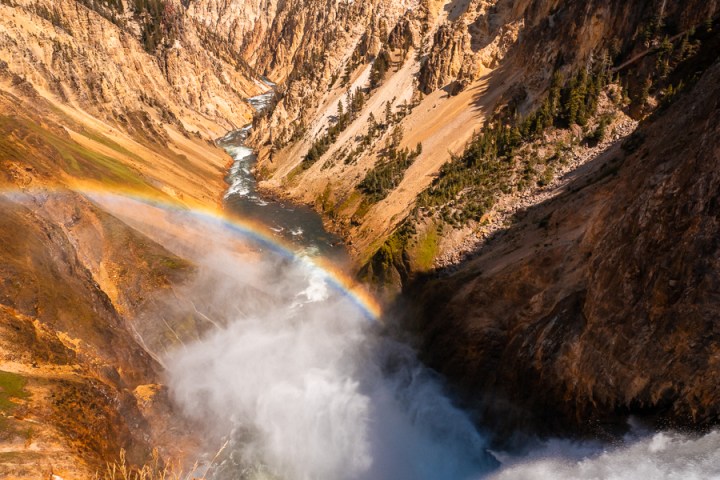 Waterfall in a canyon with rainbow and blue sky.
