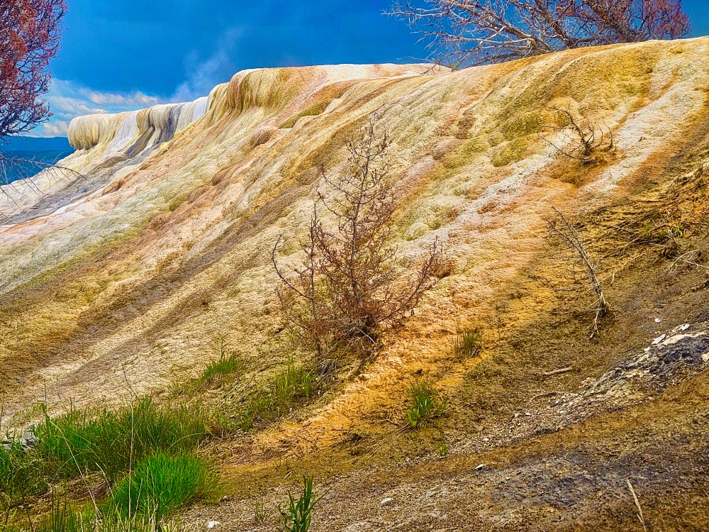 Colorful mineral rocks with sparse vegetation and cloudy sky background.