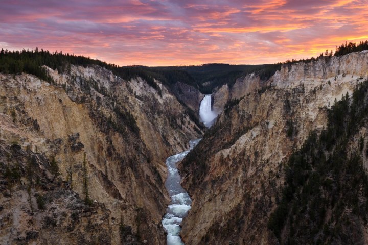 Canyon with waterfall under a vibrant sunset sky.