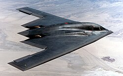 Stealth bomber aircraft flying over a desert landscape.