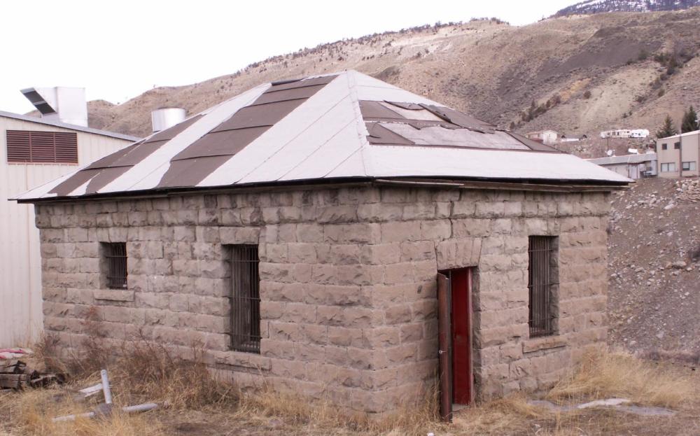 Small stone building with metal roof and barred windows, set in a mountainous area.