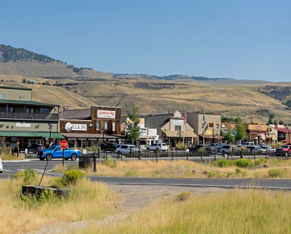 Street view of a small town with buildings, cars, and hills in the background.